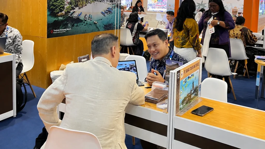 Two travel professionals discussing services over a laptop at an ITB Asia 2026 exhibition table